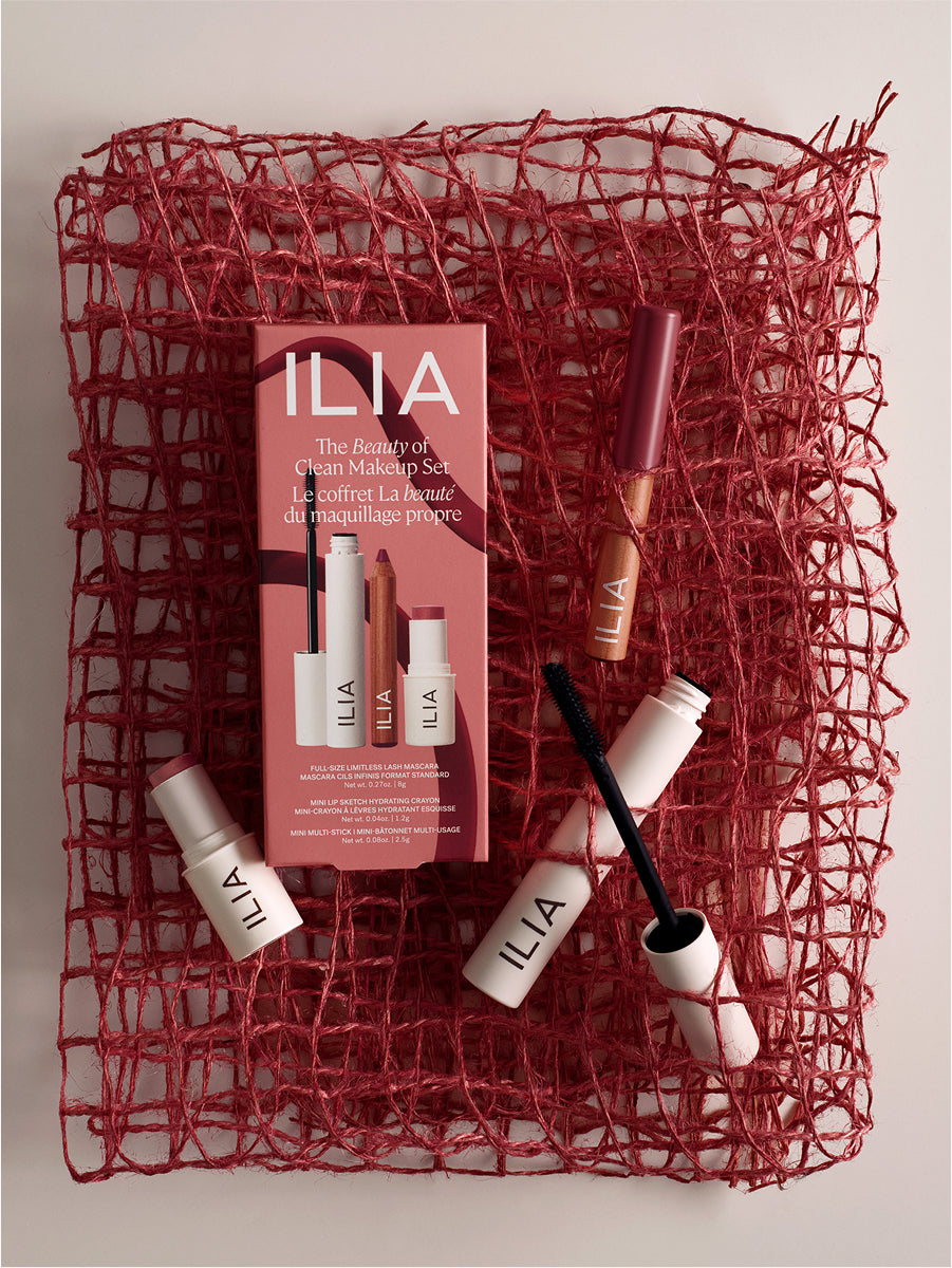 ILIA makeup set with products and packaging on a textured red surface