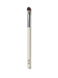 A close up of ILIA Shadow Brush that has a flat, tapered head and a white handle.